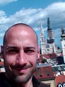 Marcio com a cidade de Zagreb por trás. Pode-se ver a catedral de Zagreb erguer-se entre vários prédios baixos.