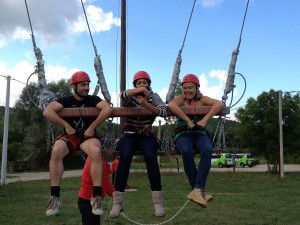 Marcio, Ashley e Violetta se agarram às toras do balanço gigante, rindo nervosamente.
