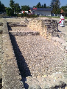 O início de muros grossos de pedra expostos ao ar livre; uma camada de cascalho ainda recobre o resto das paredes.
