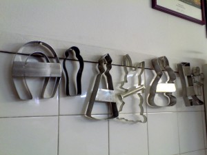 Várias formas de biscoito penduradas numa parede de azulejo, em forma de ferradura, vela, coelho, árvore...