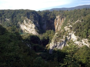 Entre montanhas rochosas cobertas de vegetação, lagos se espalham no fundo do vale. Uma comprida cachoeira está na parte direita do vale.